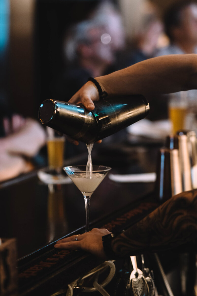 Bar tender pouring cocktail from shaker into martini glass